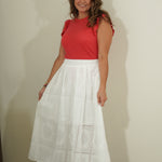 Woman wearing a red top and white skirt against a plain background