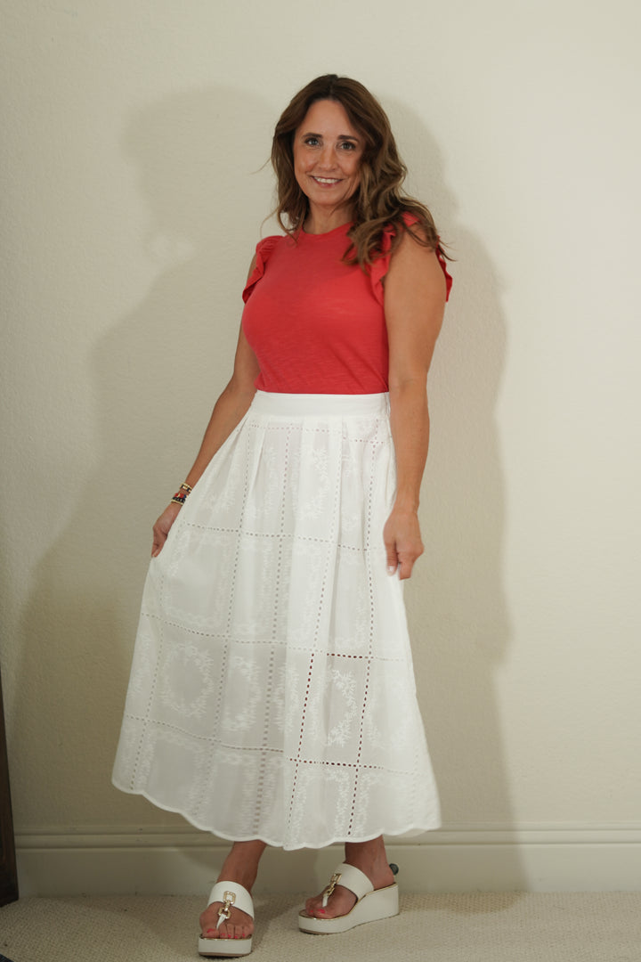 Woman wearing a red top and white skirt against a plain background