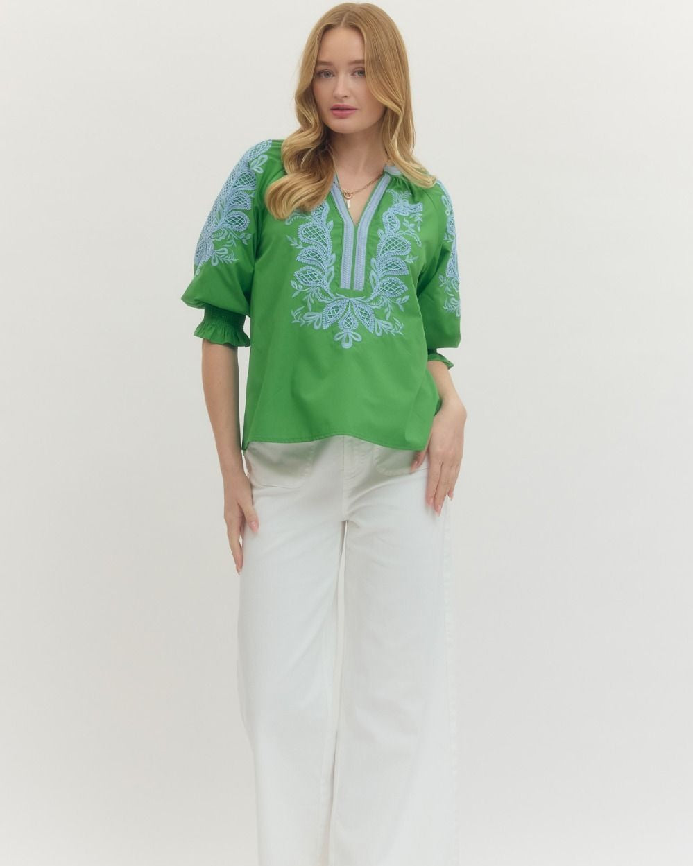 Woman wearing a green embroidered blouse with white pants on a white background