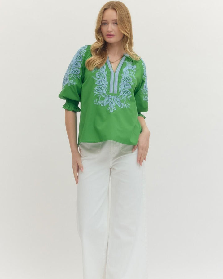 Woman wearing a green embroidered blouse with white pants on a white background