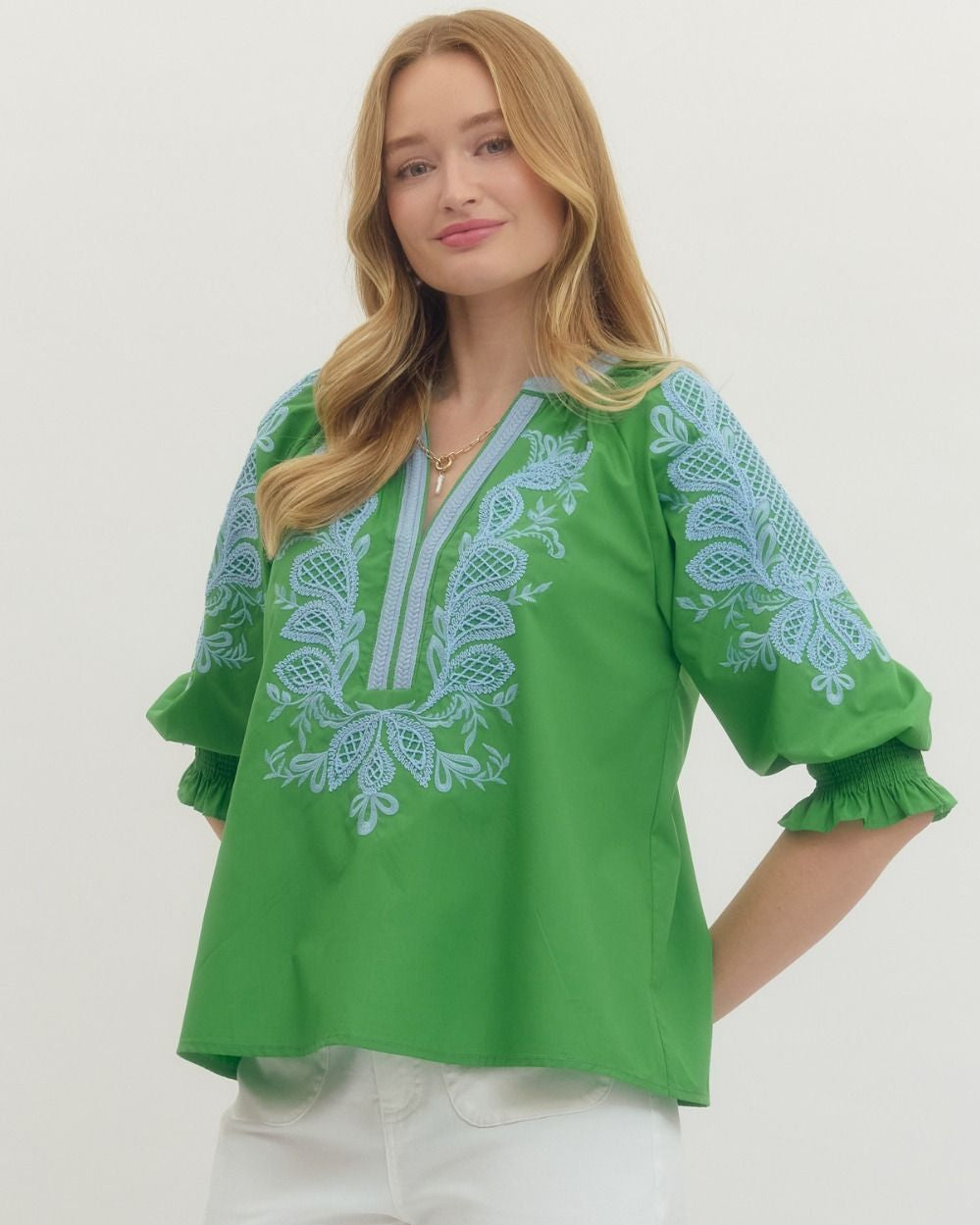 Woman wearing a green blouse with blue embroidery on a white background