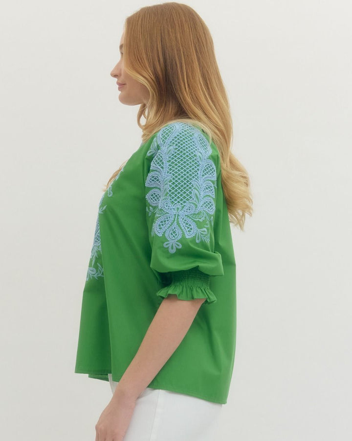 Woman wearing a green blouse with blue lace details on a white background