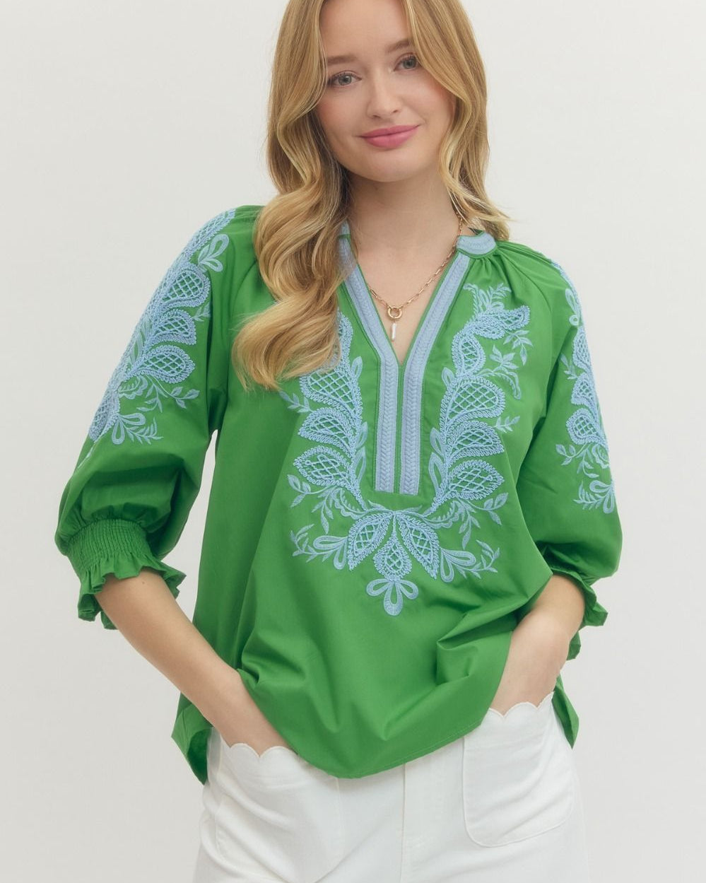 Woman wearing a green blouse with white embroidery on a plain background