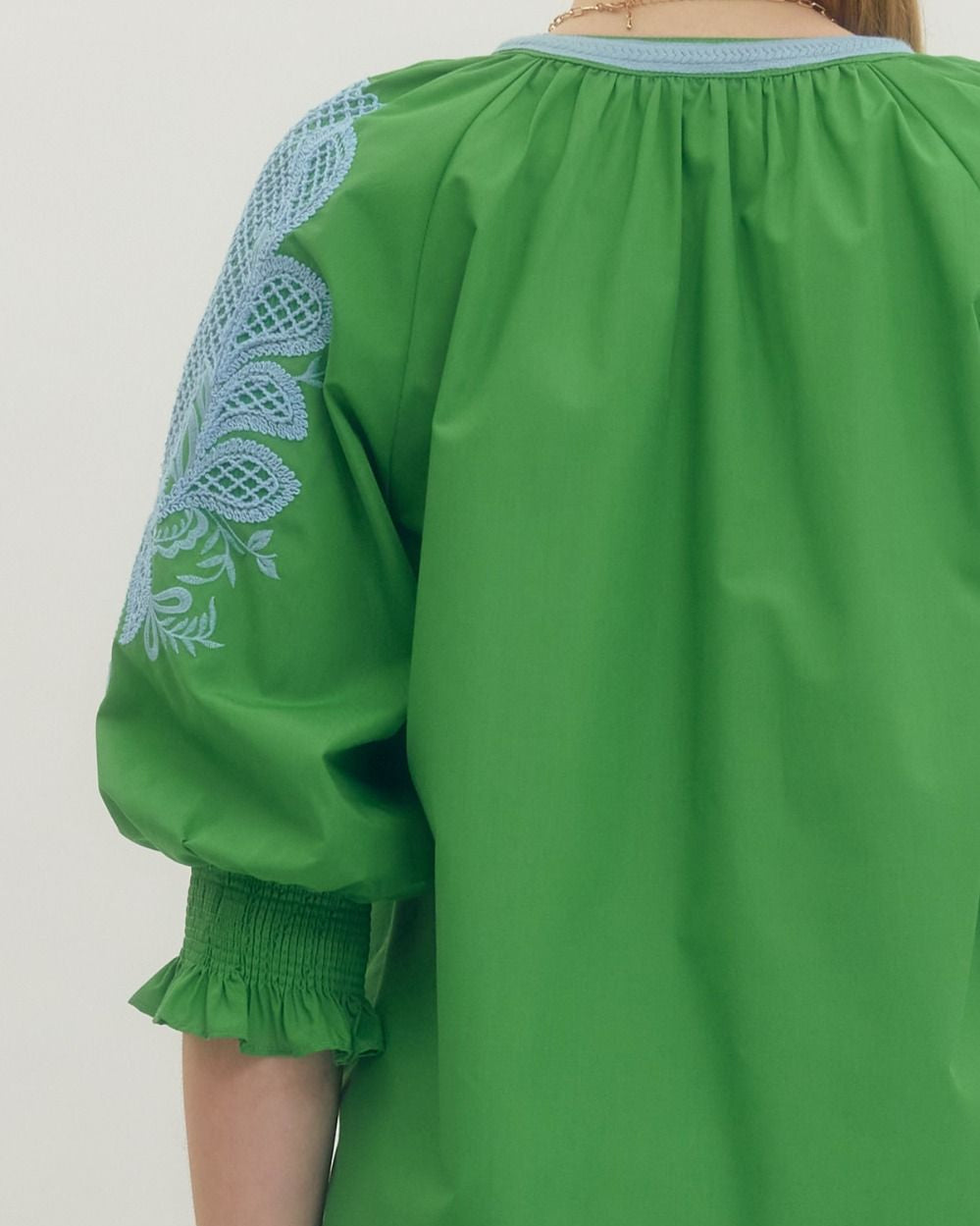 Green blouse with blue embroidery on a plain background