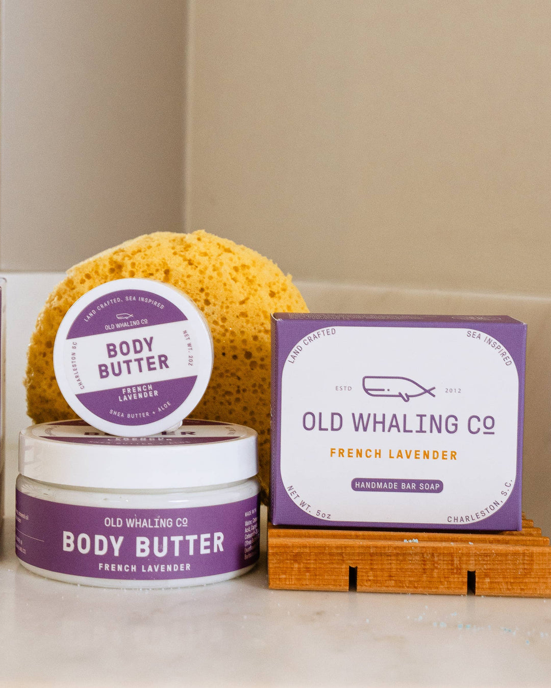 Bath products including a bath bomb, body butter, and a candle on a white surface with a beige background.