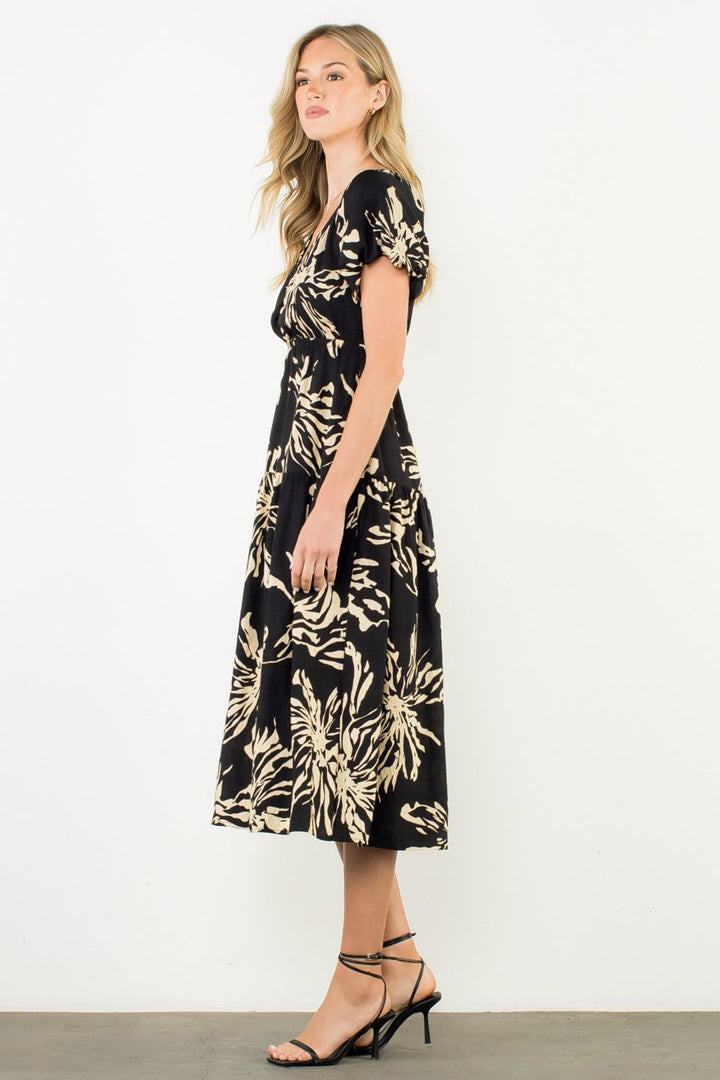 Woman wearing a black dress with gold floral pattern on a white background