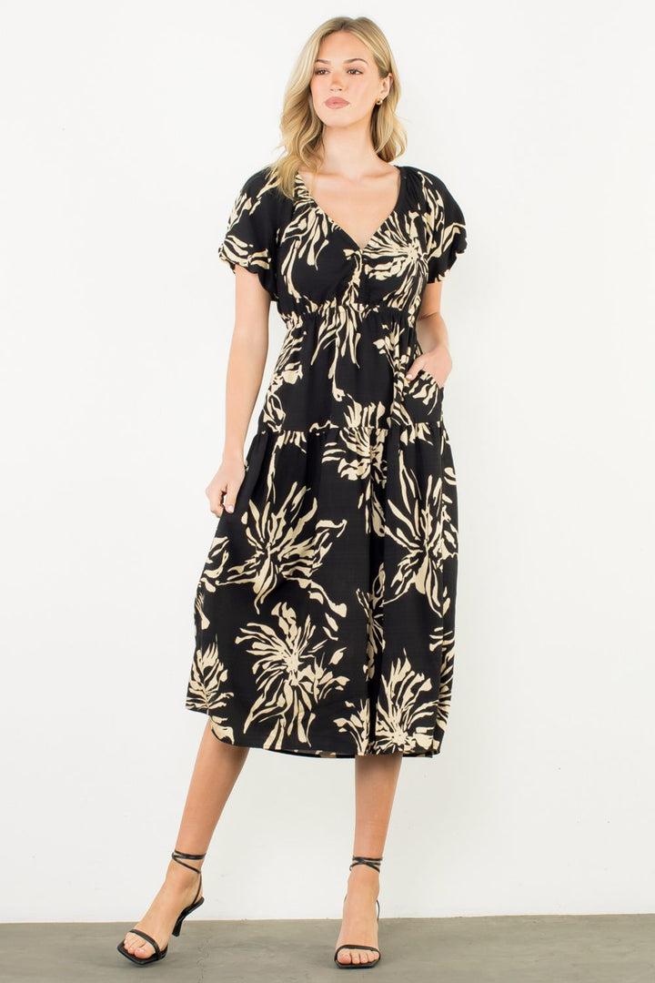 Woman wearing a black dress with gold floral pattern against a white background