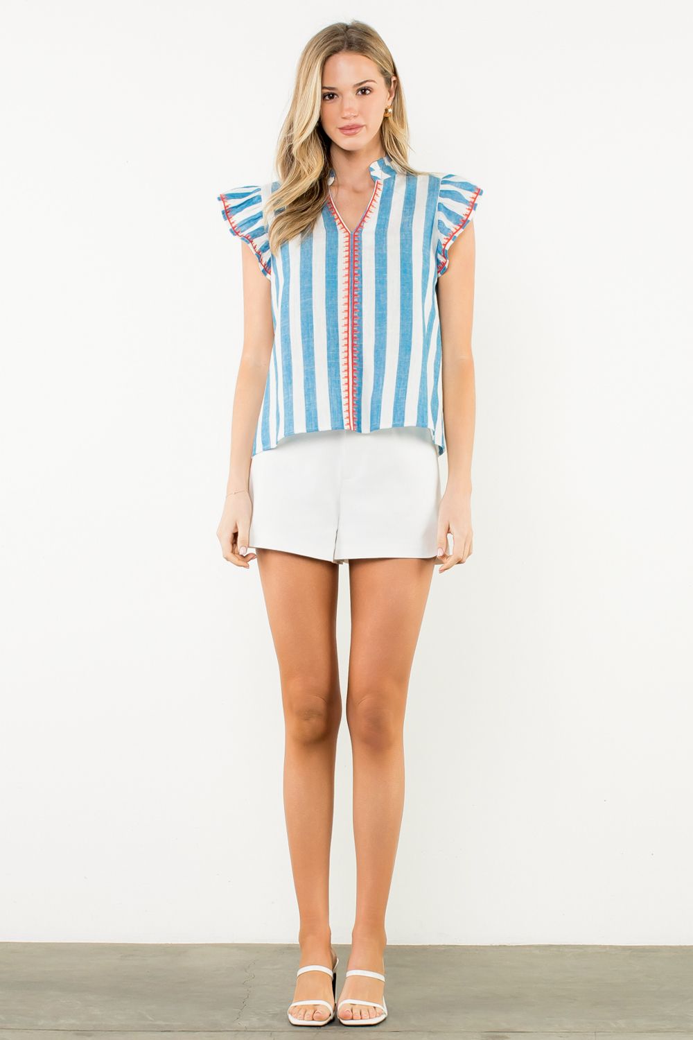 Woman wearing a striped shirt and white shorts on a plain background