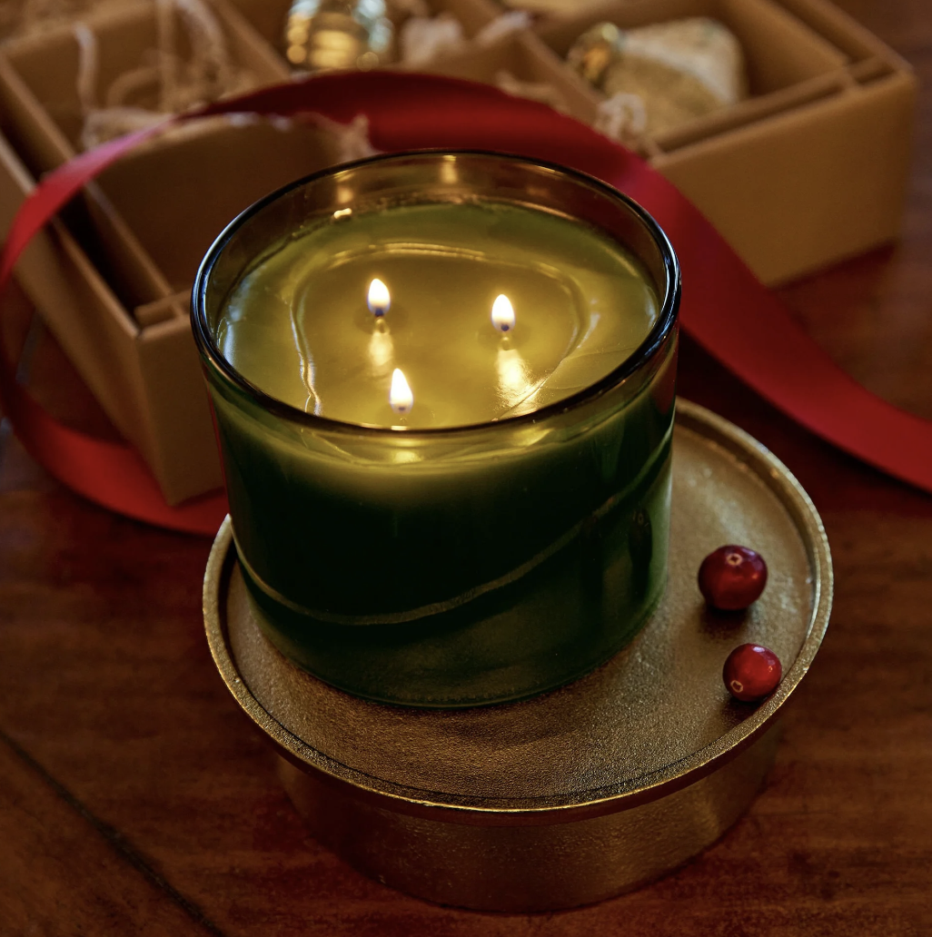 Green candle with three flames on a wooden coaster, with a blurred background