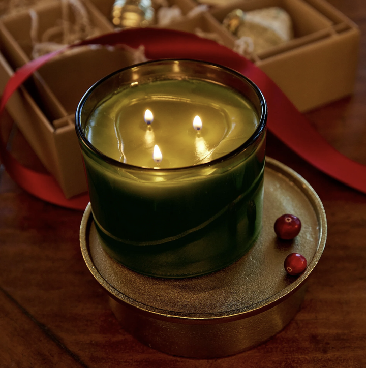 Green candle with three flames on a wooden coaster, with a blurred background
