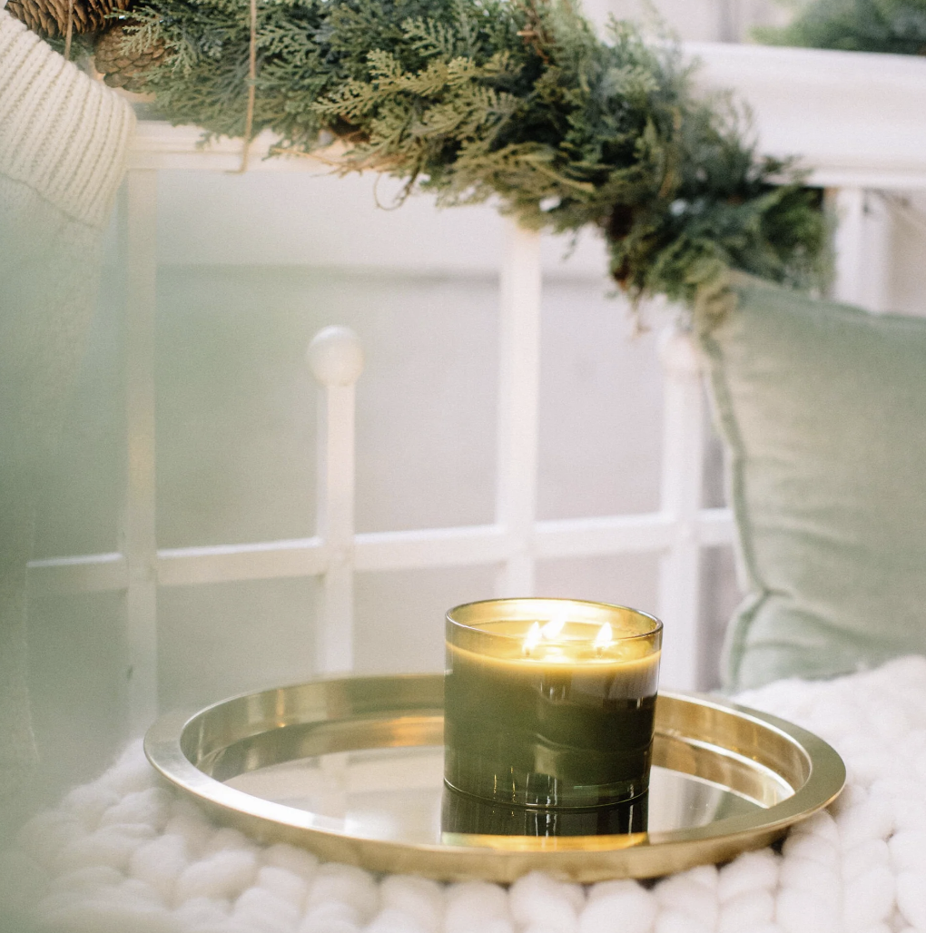 Candle on a gold tray with greenery in the background
