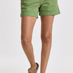 A pair of green,Dear John Hampton shorts with a slightly low-rise waist and tailored fit around the hips and thighs. The shorts have a cuffed hem and slanted side pockets, worn with a white top and tan sandals.