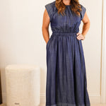Woman in a blue dress standing in a room with white walls and furniture.