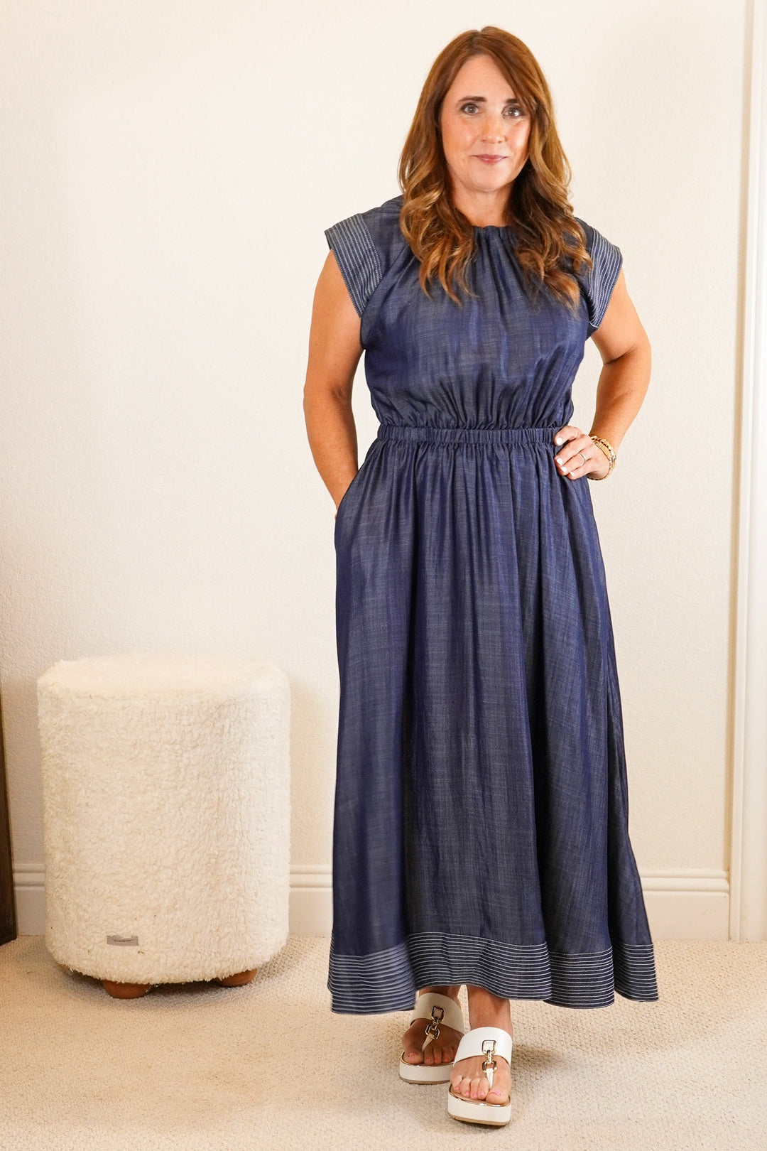 Woman in a blue dress standing in a room with white walls and furniture.