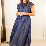 Woman in a blue dress standing in a room with white walls and furniture.