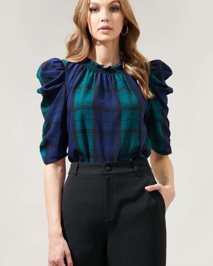 Woman wearing a plaid blouse with ruffled sleeves against a plain background