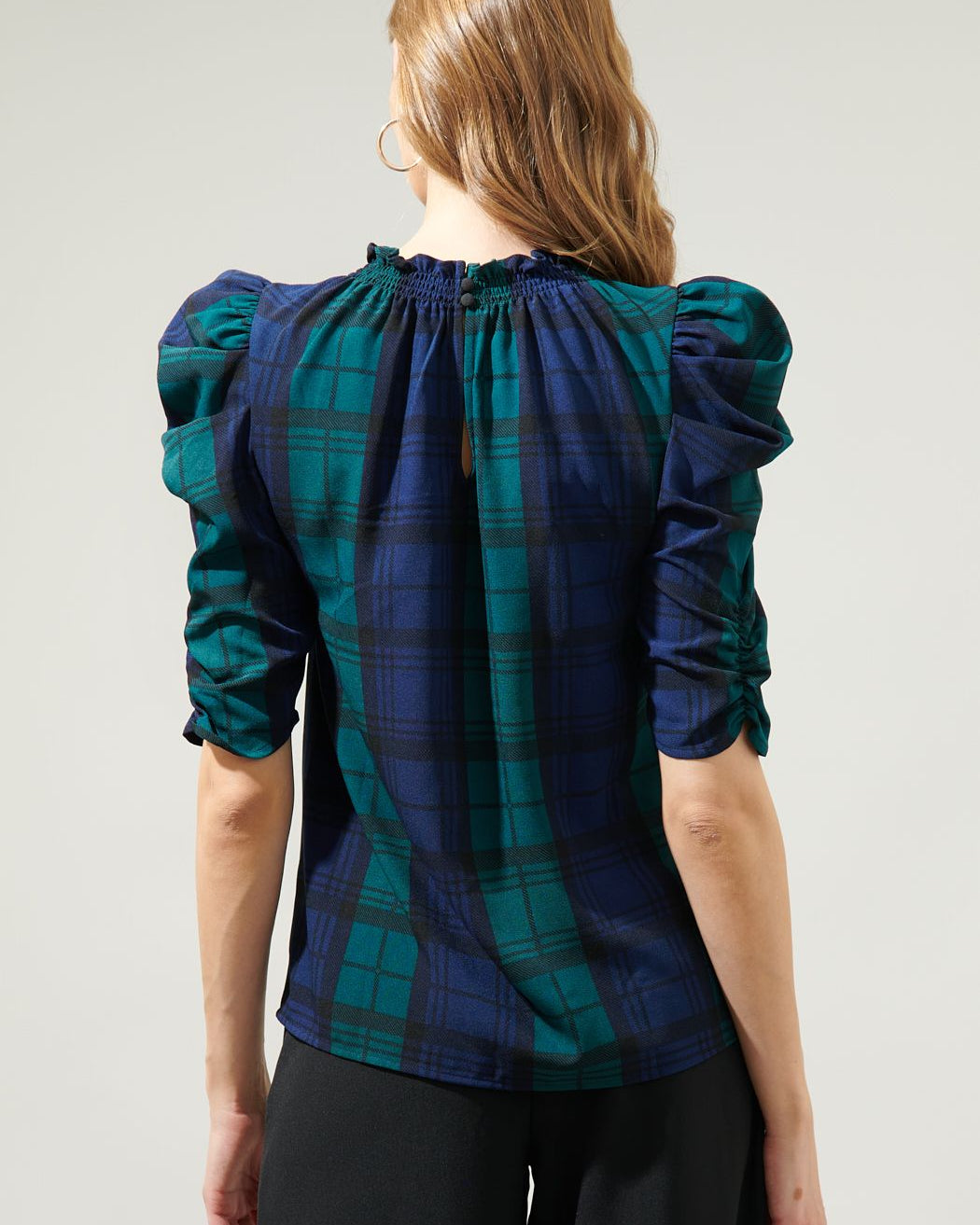 Woman wearing a blue and green plaid blouse with puffed sleeves on a light gray background