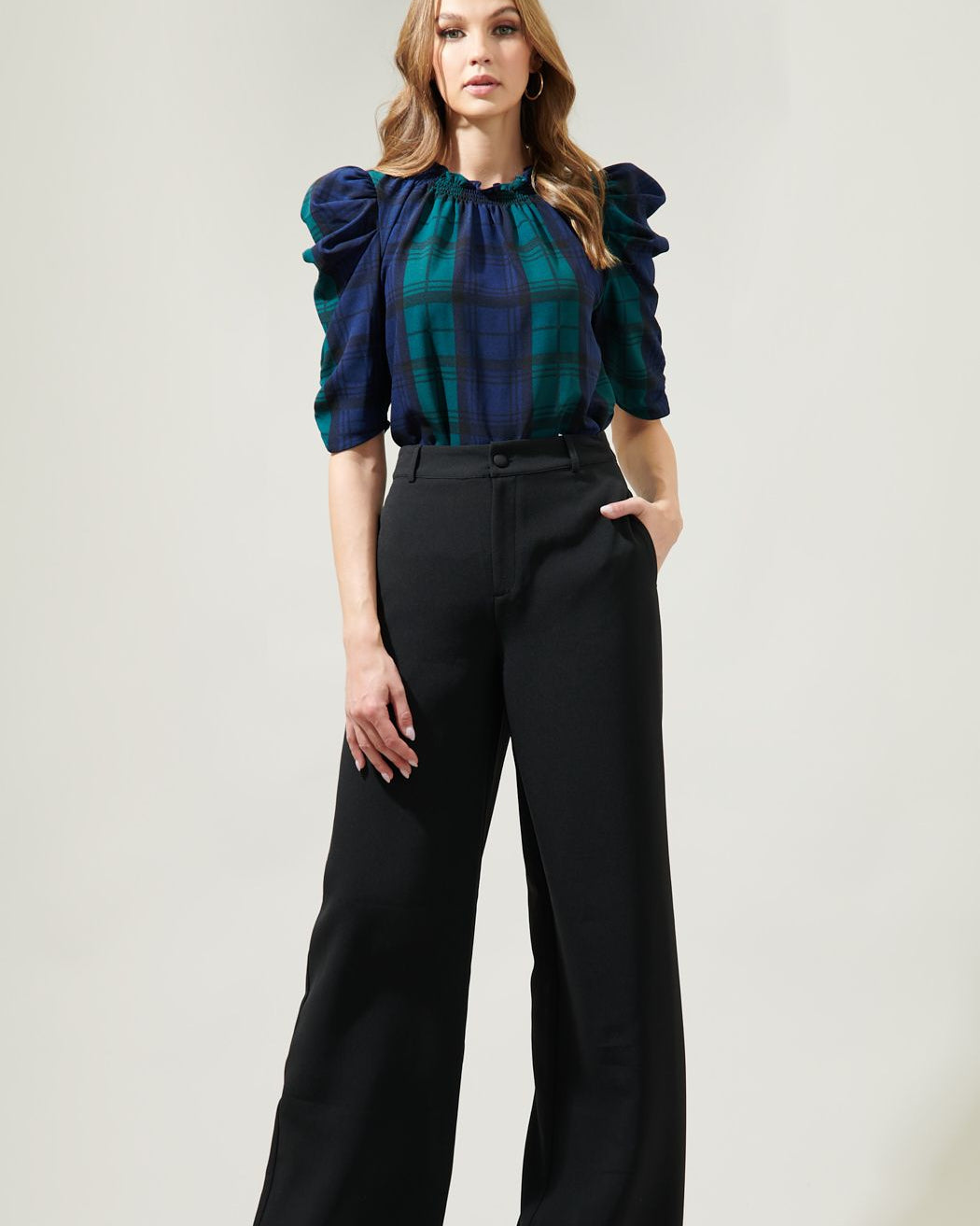 Woman wearing a blue and green plaid blouse with black pants on a white background