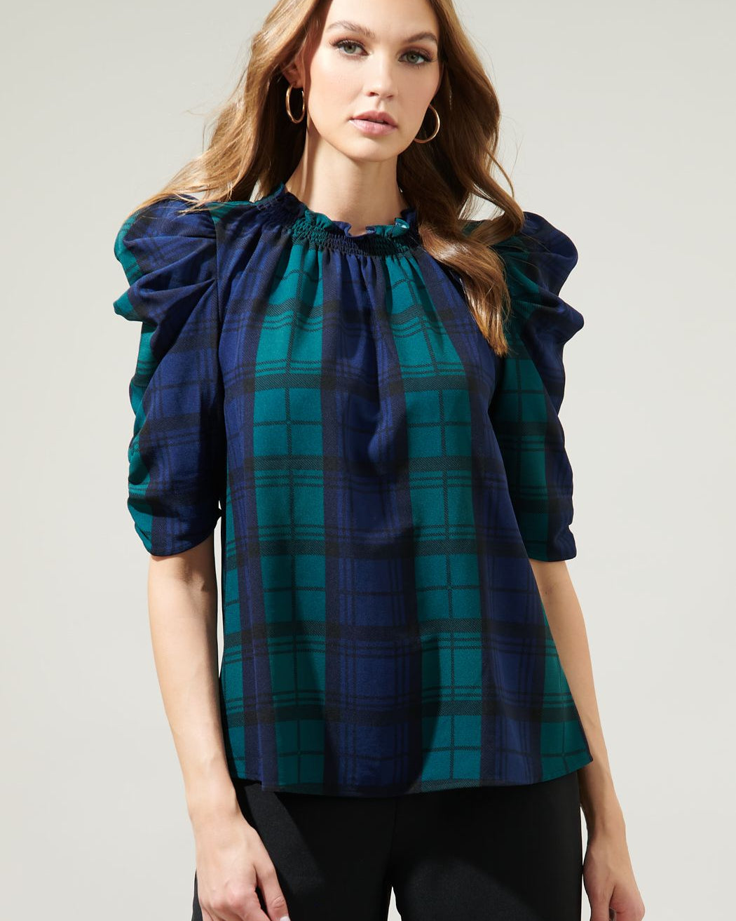Woman wearing a blue and green plaid blouse with ruffled sleeves on a gray background