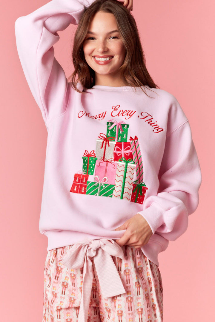 Person wearing a pink sweatshirt with Christmas-themed design on a pink background
