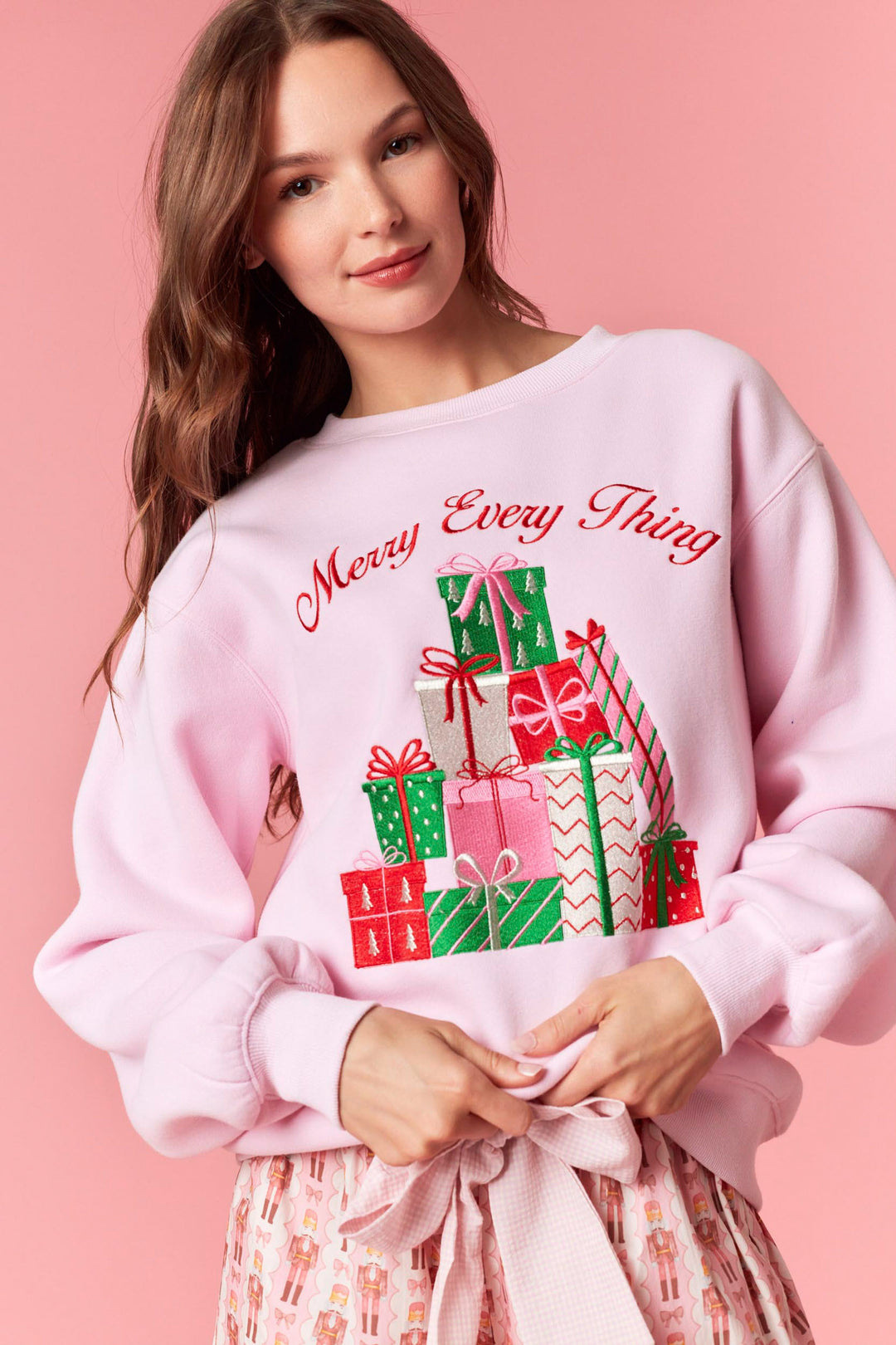 Woman wearing a pink sweatshirt with Christmas-themed design on a pink background