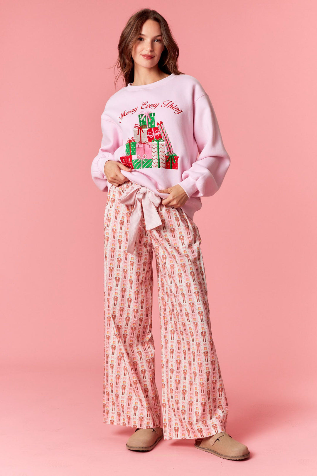 Woman wearing a pink Christmas-themed sweatshirt and patterned pants on a pink background