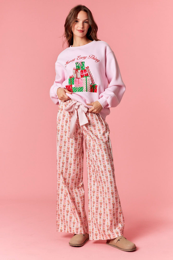 Woman wearing a pink Christmas-themed sweatshirt and patterned pants on a pink background