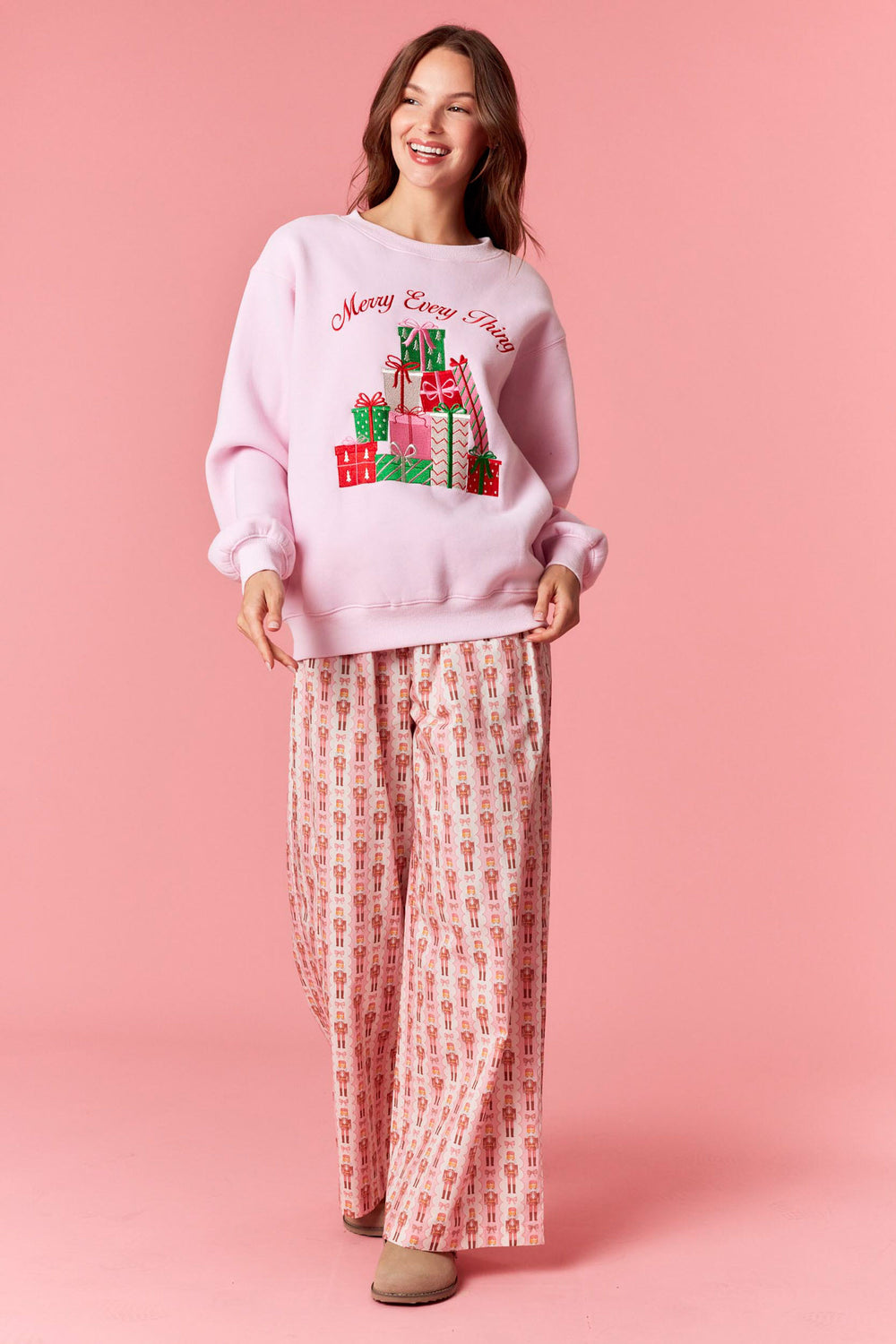 Woman wearing a pink 'Merry Christmas' sweater with gift designs on a pink background