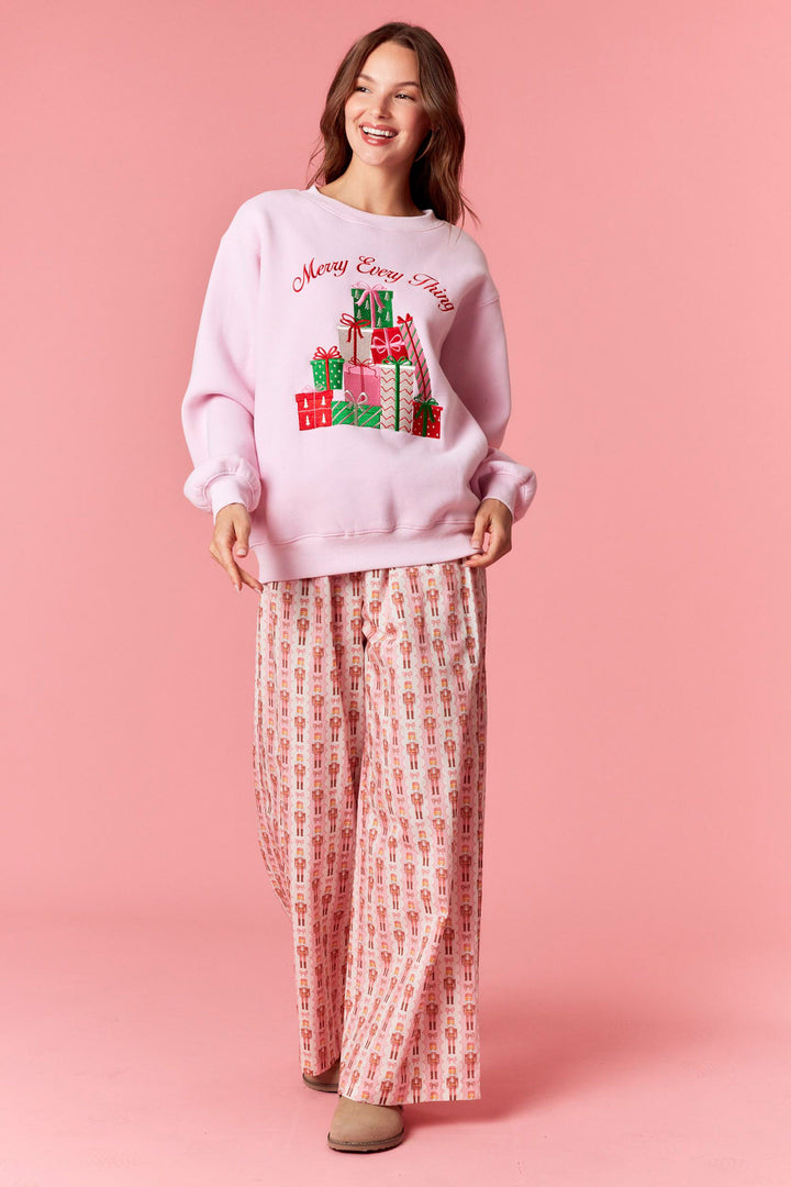 Woman wearing a pink 'Merry Christmas' sweater with gift designs on a pink background