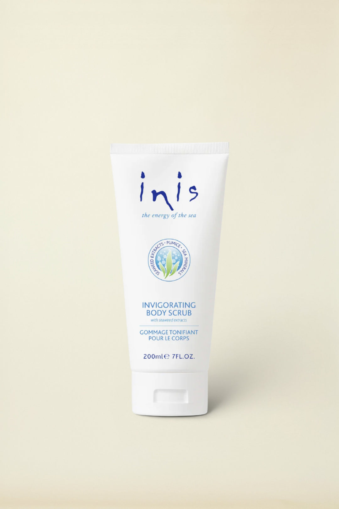 A white squeeze tube of Inis Invigorating Body Scrub with blue text, centered on a warm cream background.