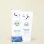 Inis Invigorating Body Scrub shown in a white squeeze tube next to its matching white and blue packaging box, set against a solid light beige background.