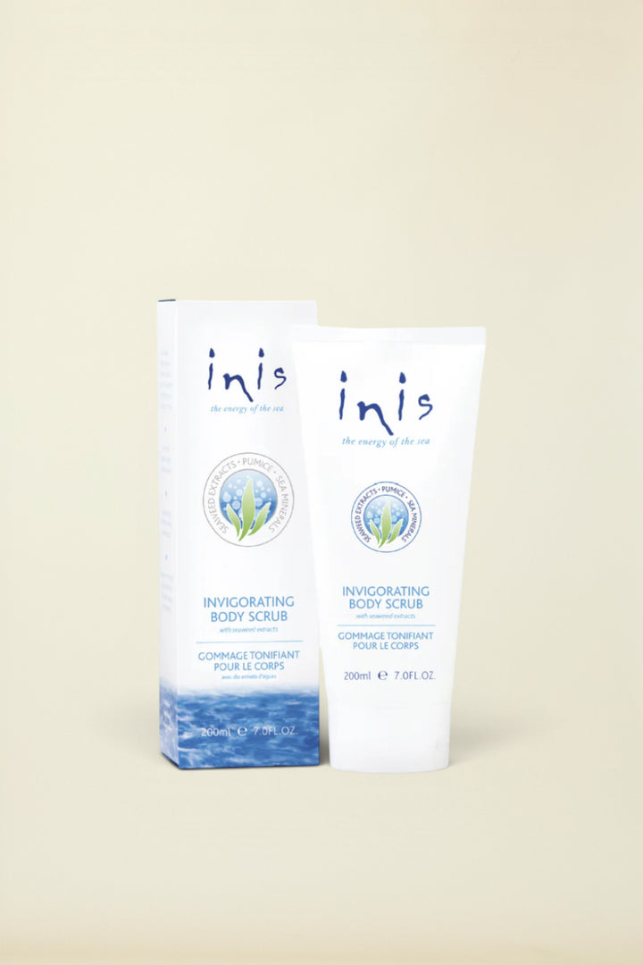 Inis Invigorating Body Scrub shown in a white squeeze tube next to its matching white and blue packaging box, set against a solid light beige background.