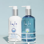 Two Inis Sea Mineral hand wash and hand lotion bottles displayed in a white wire basket on a bathroom counter. The left bottle is white with blue text, and the right bottle is translucent blue with a silver cap.