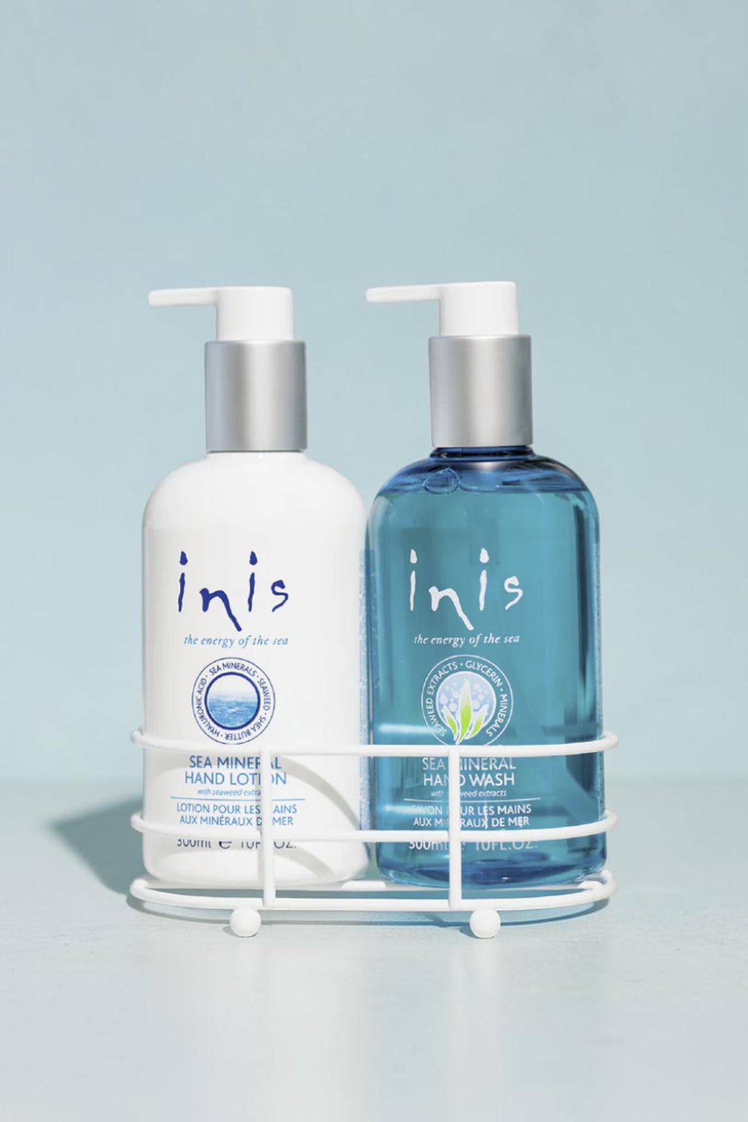Two Inis Sea Mineral hand wash and hand lotion bottles displayed in a white wire basket on a bathroom counter. The left bottle is white with blue text, and the right bottle is translucent blue with a silver cap.