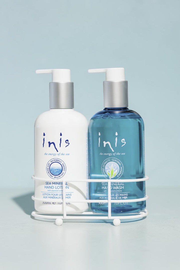 Two Inis Sea Mineral hand wash and hand lotion bottles displayed in a white wire basket on a bathroom counter. The left bottle is white with blue text, and the right bottle is translucent blue with a silver cap.
