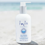 A 300ml bottle of Inis Sea Mineral Hand Lotion on a light marble surface, styled with a dollop of white lotion, a woven tray, and a blurred potted plant in the background.