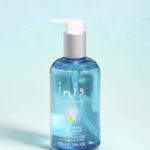 A bottle of Inis Mineral Hand Wash with a white pump dispenser and blue liquid, styled on a white surface with decorative blue crystals and a blurred bathroom background.