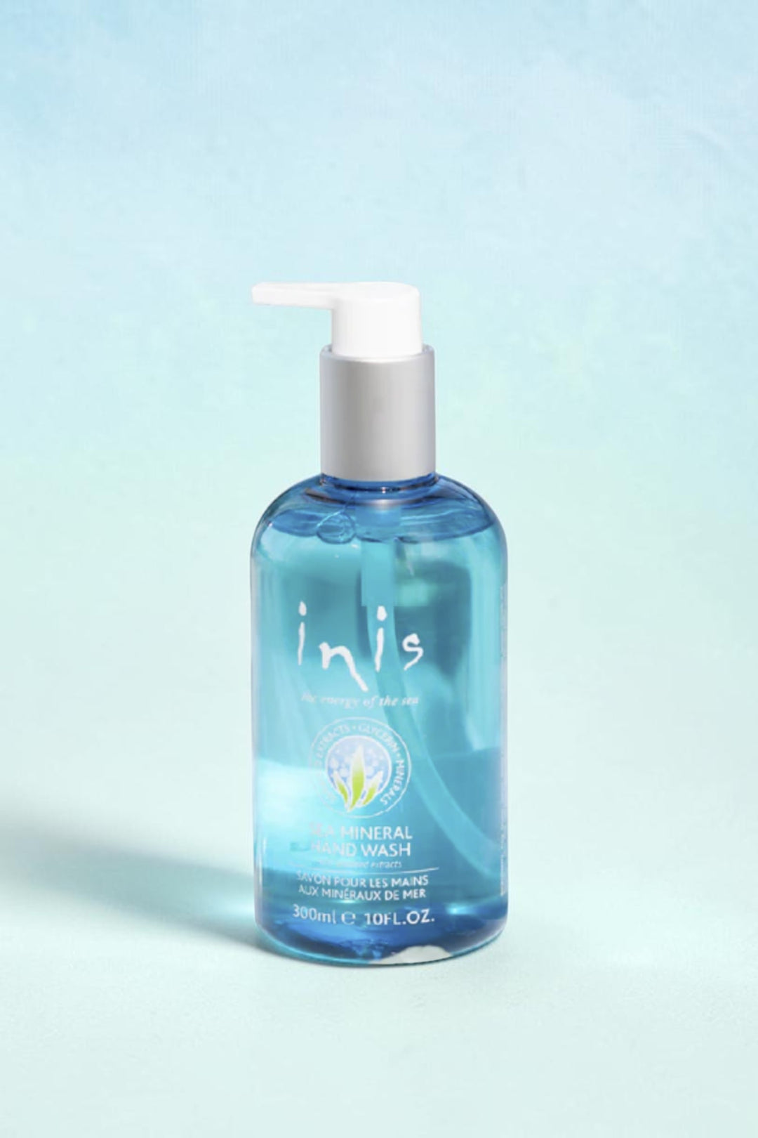A bottle of Inis Mineral Hand Wash with a white pump dispenser and blue liquid, styled on a white surface with decorative blue crystals and a blurred bathroom background.