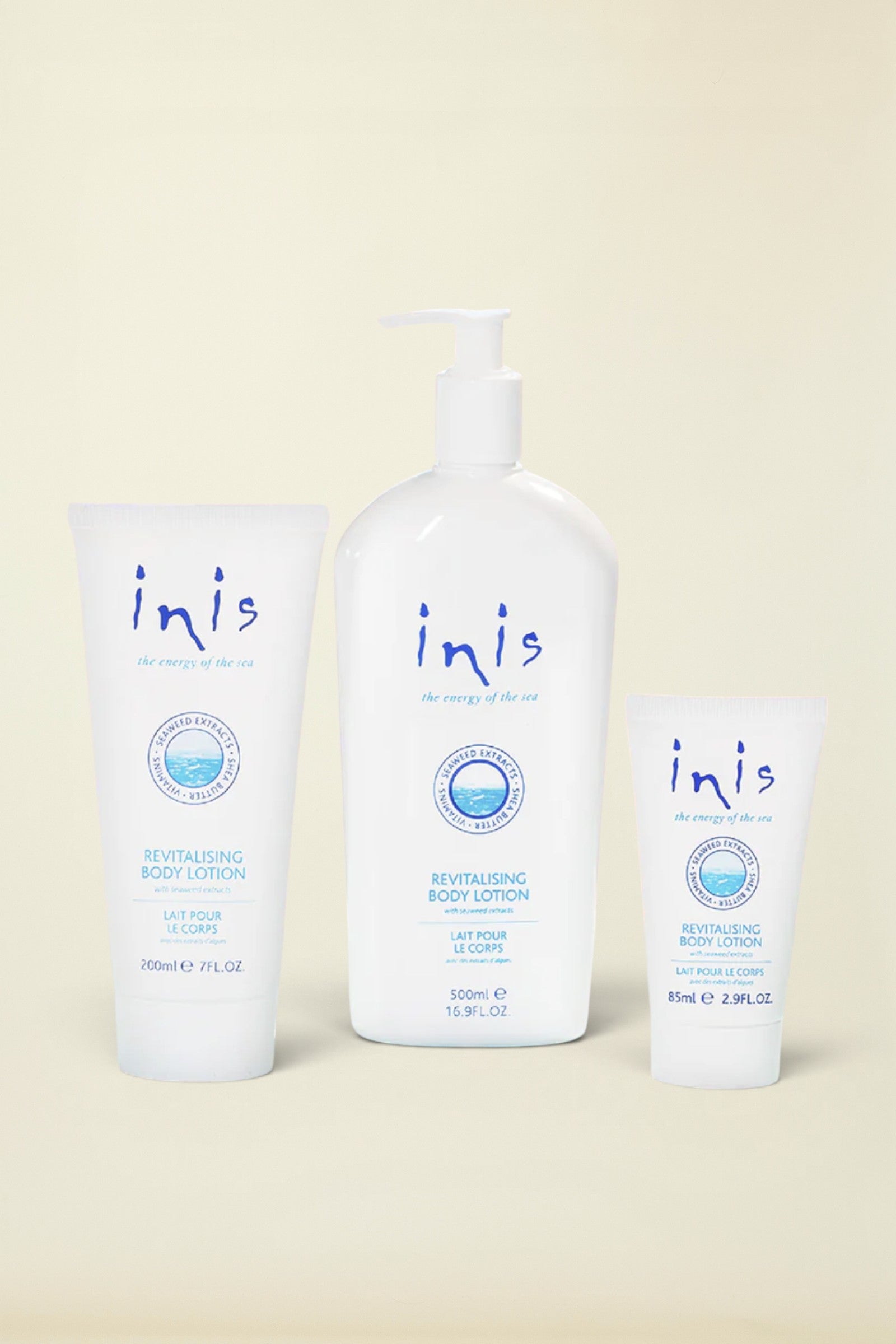 Three white Inis Revitalising Body Lotion containers on a light blue background: a 200ml squeeze tube, a 120ml pump bottle, and a 8ml travel tube, with a small silver foil pack at the lower left.