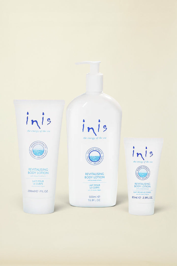 Three white Inis Revitalising Body Lotion containers on a light blue background: a 200ml squeeze tube, a 120ml pump bottle, and a 8ml travel tube, with a small silver foil pack at the lower left.