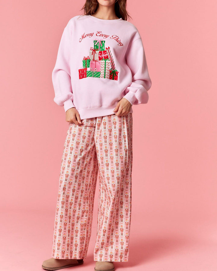 Woman wearing a pink Christmas-themed sweater and patterned pants on a pink background