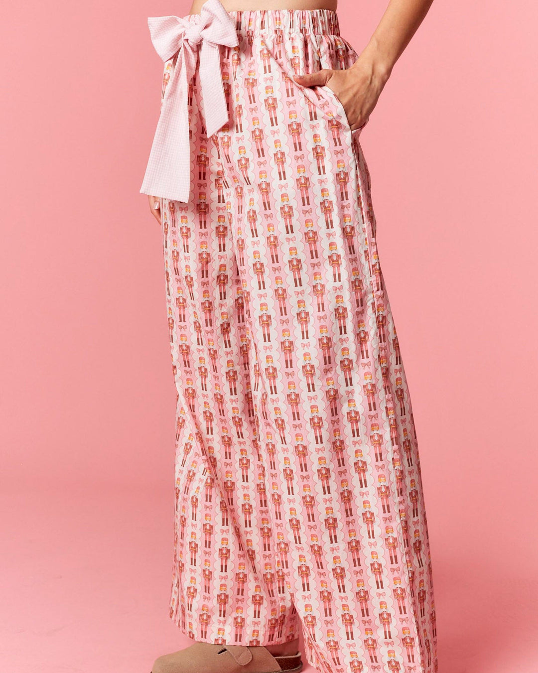 Person wearing a patterned pink and white outfit with a bow on a pink background