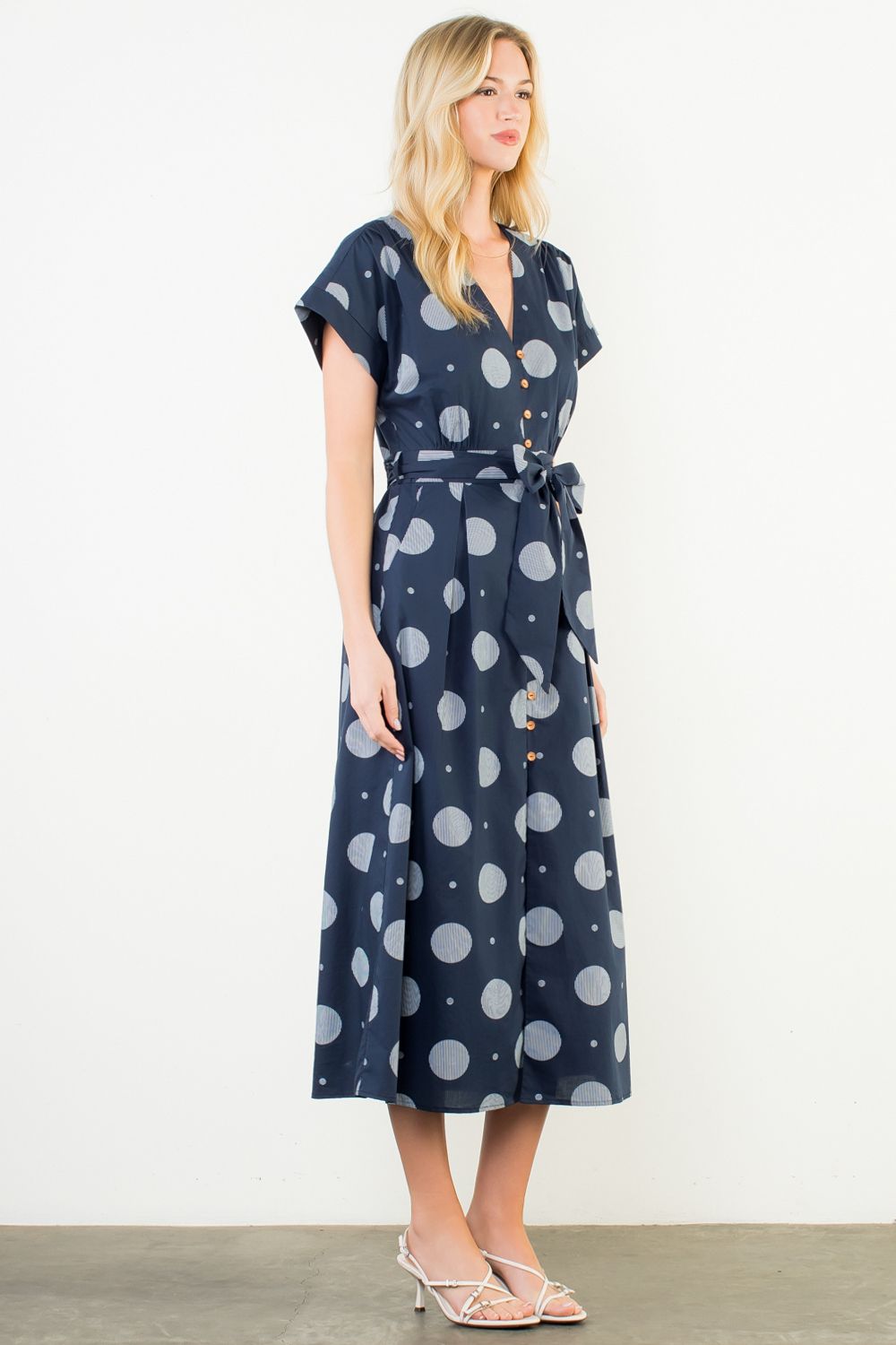 Woman wearing a navy dress with gray polka dots on a white background