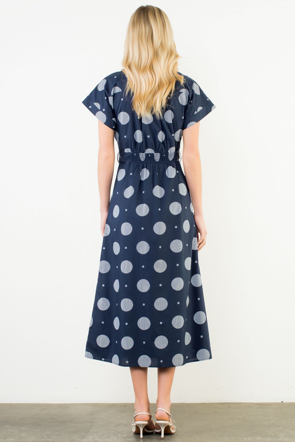 Woman wearing a navy dress with white polka dots against a white background