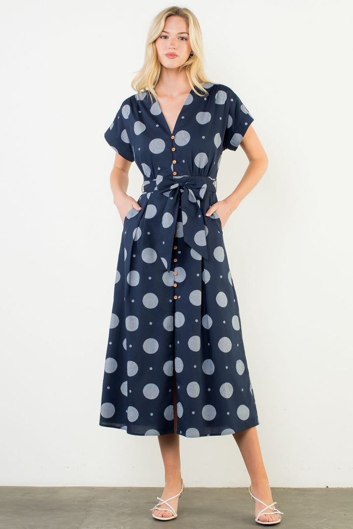 Woman wearing a navy dress with white polka dots against a white background