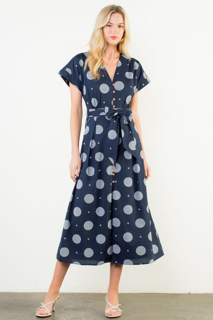 Woman wearing a navy dress with white polka dots against a white background