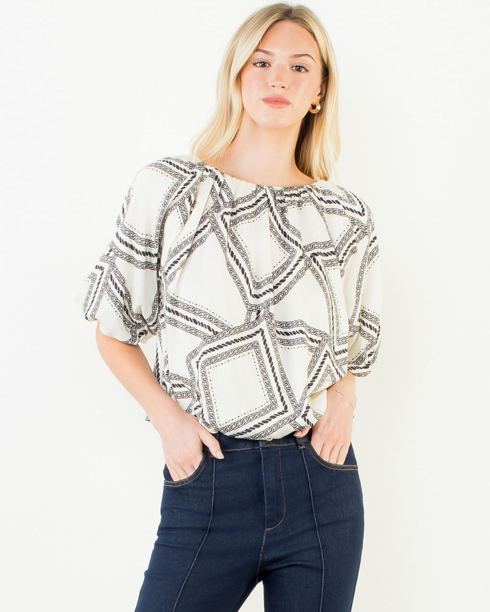 Woman wearing a patterned top and dark jeans on a white background