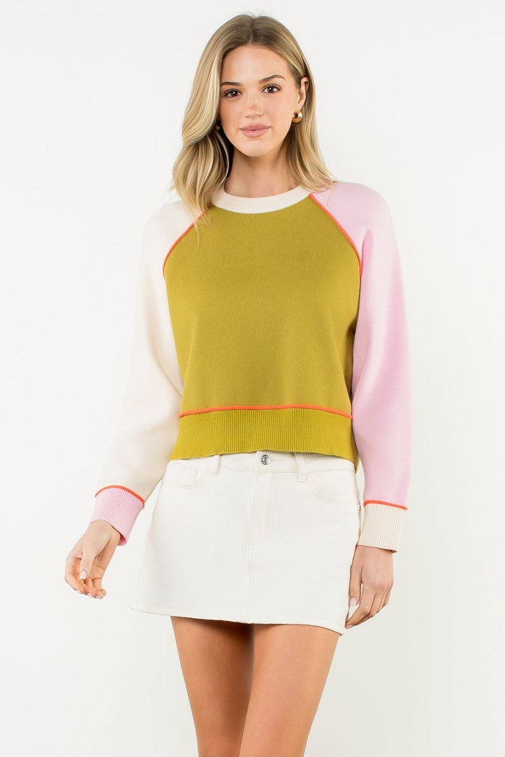 Lindsey Sweater - Woman wearing a colorful sweater with pink sleeves and a green body on a white 