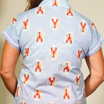 Person wearing a shirt with lobster pattern and orange pants against a neutral background