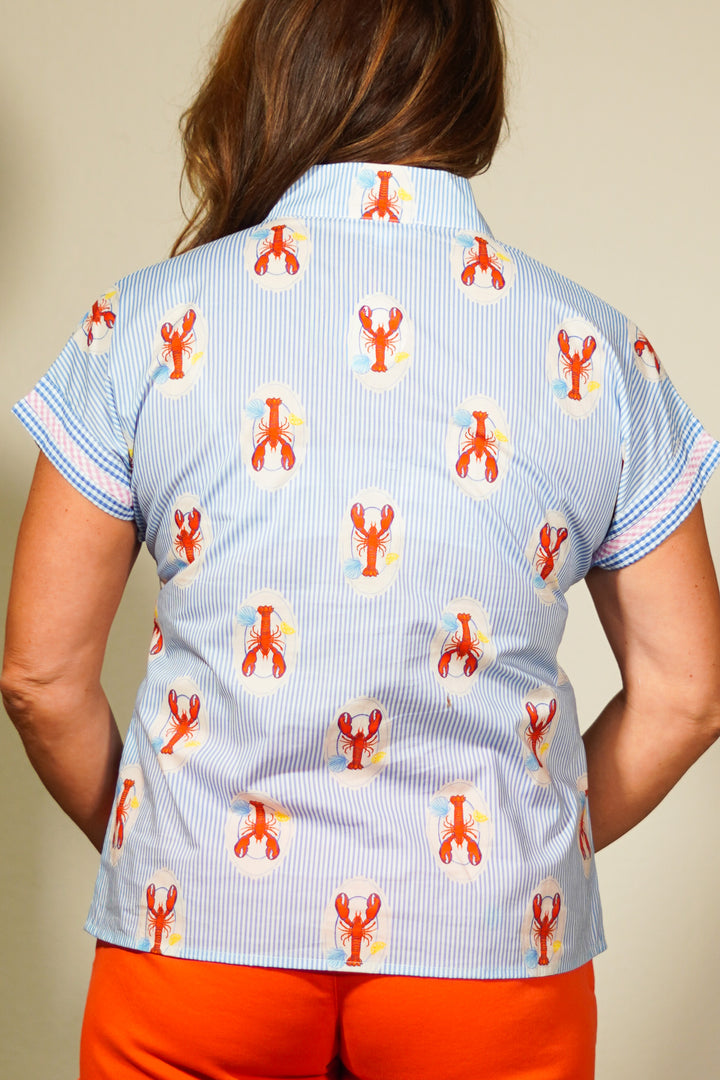 Person wearing a shirt with lobster pattern and orange pants against a neutral background